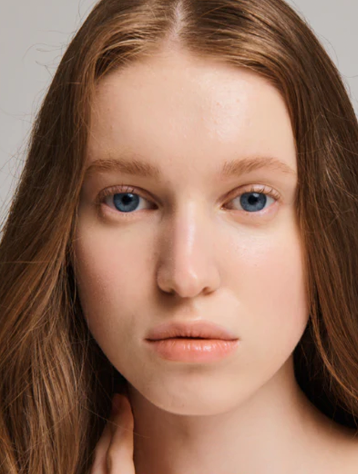 a young woman with striking blue eyes and naturally highlighted skin, her delicate features and subtle makeup enhancing her serene and natural beauty
