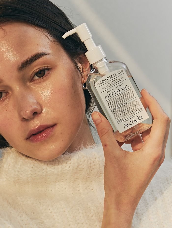 A close-up of a person holding a bottle of Arencia Phyto-Oil, highlighting the product's skincare benefits and sleek packaging